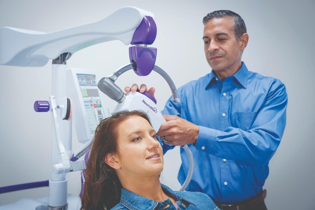 Healthcare provider positioning a magnetic therapy coil near a seated patient's head in a clinic room.